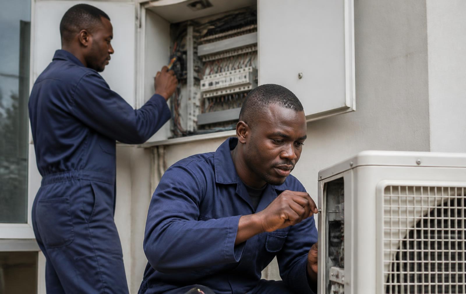 Dois técnicos de manutenção a intervir num quadro eléctrico e numa unidade de climatização